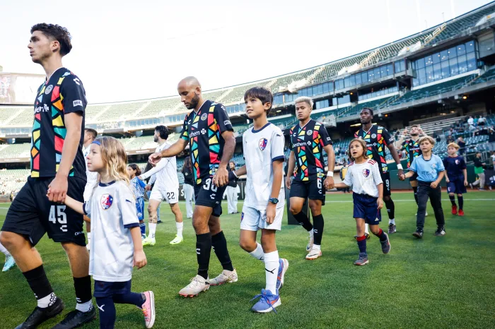 Les joueurs du Oakland Roots SC escortés sur le terrain par des enfants locaux.