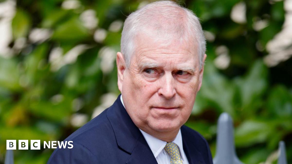 Image of Andrew Mountbatten Windsor. He is looking off to the right. Andrew has thinning grey hair and is wearing a navy suit jacket, white shirt and a yellow patterned tie