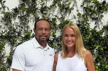 Tiger Woods et Vanessa Trump souriant devant un mur blanc avec des plantes vertes